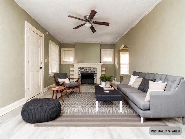 living room with wood-type flooring, a stone fireplace, ceiling fan, and crown molding