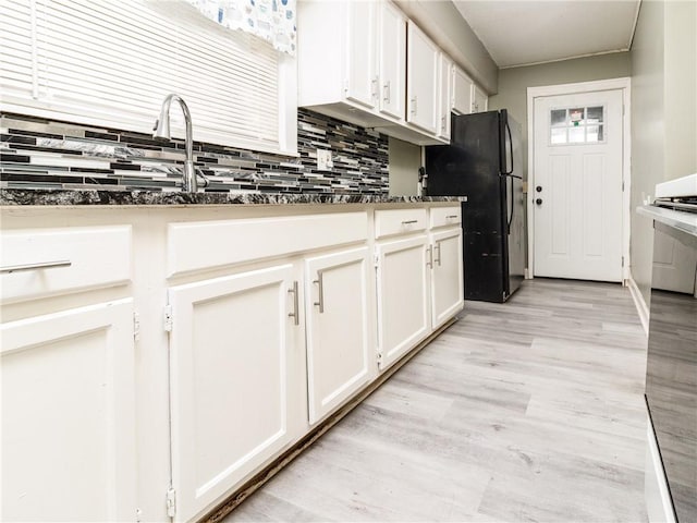 kitchen with decorative backsplash, light hardwood / wood-style floors, black refrigerator, and white cabinetry