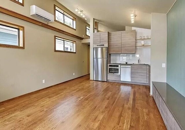 kitchen featuring appliances with stainless steel finishes, a wall mounted AC, sink, high vaulted ceiling, and light hardwood / wood-style flooring