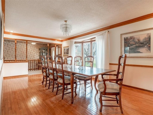 dining space with light wood-type flooring, a textured ceiling, ornamental molding, and a notable chandelier