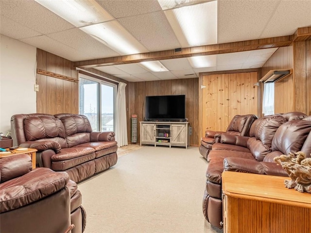 carpeted living room featuring a drop ceiling and wooden walls