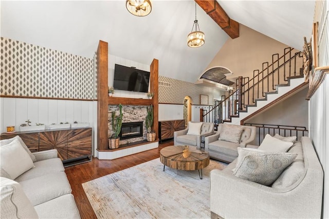 living room with beam ceiling, a stone fireplace, hardwood / wood-style floors, and an inviting chandelier