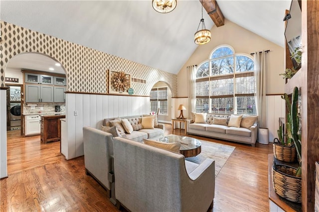 living room with lofted ceiling with beams, light hardwood / wood-style floors, washer / dryer, and a chandelier