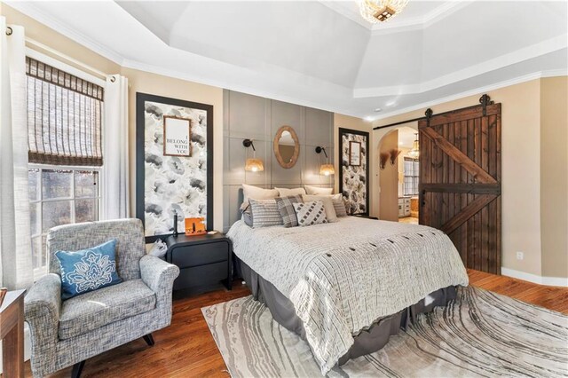 bedroom featuring dark hardwood / wood-style floors, a barn door, ornamental molding, and a tray ceiling