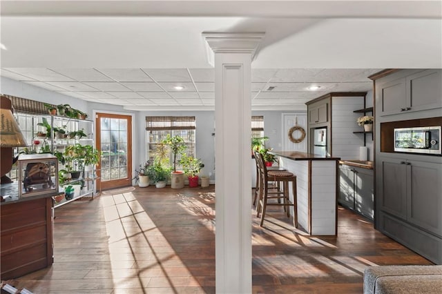 interior space featuring a paneled ceiling, decorative columns, dark wood-type flooring, and wood walls