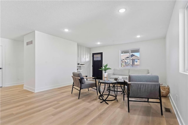 living room featuring light wood finished floors, visible vents, baseboards, recessed lighting, and a textured ceiling