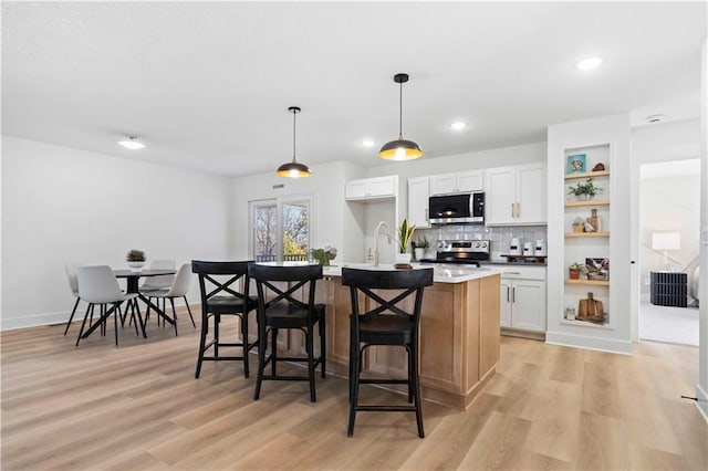 kitchen with an island with sink, decorative backsplash, light wood-style floors, appliances with stainless steel finishes, and white cabinetry