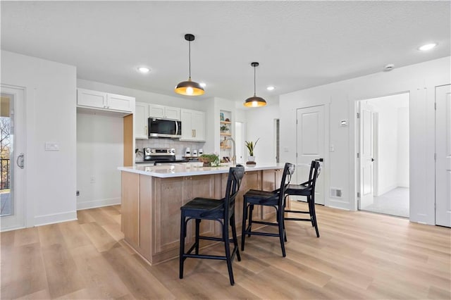 kitchen featuring light wood-style flooring, stainless steel appliances, light countertops, decorative light fixtures, and tasteful backsplash