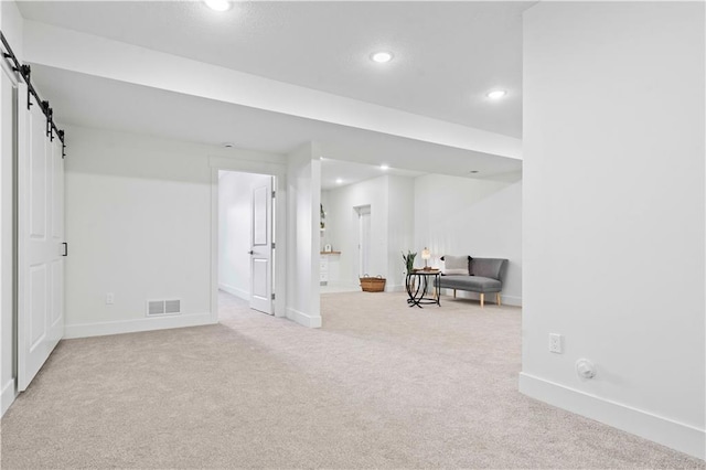 below grade area with visible vents, baseboards, carpet, a barn door, and recessed lighting