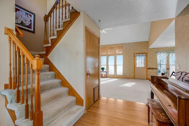 stairway featuring a textured ceiling, ceiling fan, hardwood / wood-style floors, and vaulted ceiling