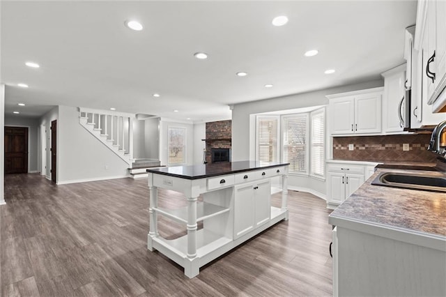 kitchen with wood finished floors, a kitchen island, a sink, open floor plan, and a brick fireplace