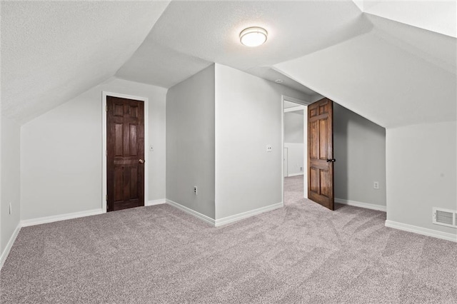 additional living space with a textured ceiling, vaulted ceiling, visible vents, and baseboards