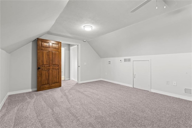 additional living space with lofted ceiling, light colored carpet, visible vents, a ceiling fan, and baseboards