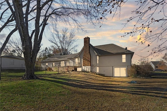 rear view of house featuring fence, a chimney, and a lawn