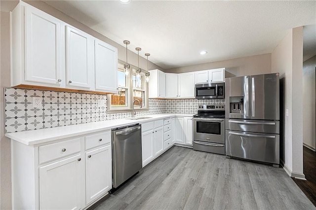 kitchen featuring appliances with stainless steel finishes, sink, decorative light fixtures, light hardwood / wood-style flooring, and white cabinetry