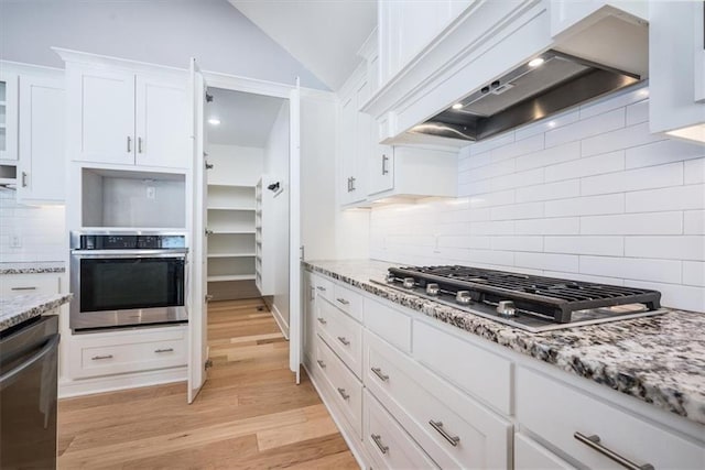 kitchen with white cabinetry, light hardwood / wood-style floors, vaulted ceiling, appliances with stainless steel finishes, and custom exhaust hood