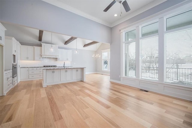 kitchen featuring decorative backsplash, light wood-type flooring, white cabinets, hanging light fixtures, and an island with sink