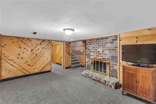 unfurnished living room with light carpet, a brick fireplace, and wooden walls