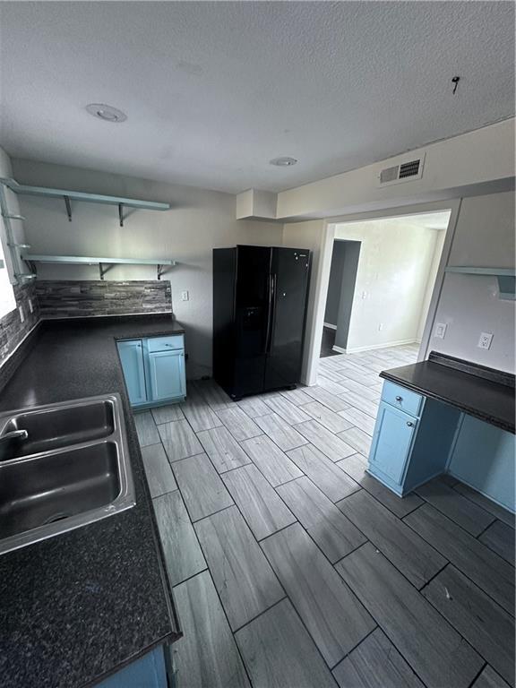 kitchen featuring a textured ceiling, blue cabinets, sink, and black refrigerator with ice dispenser