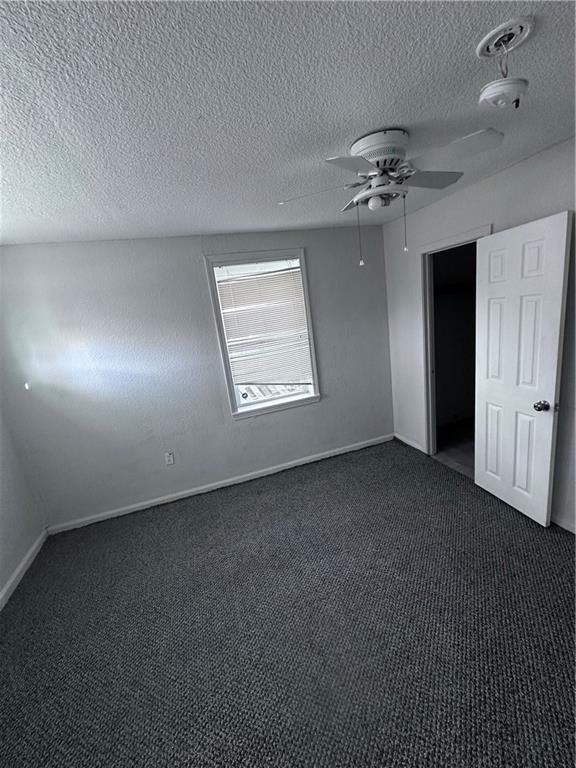 empty room with dark carpet and a textured ceiling