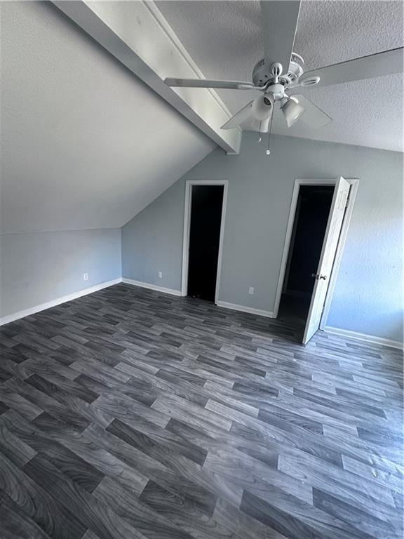 additional living space with a textured ceiling, lofted ceiling with beams, dark hardwood / wood-style floors, and ceiling fan