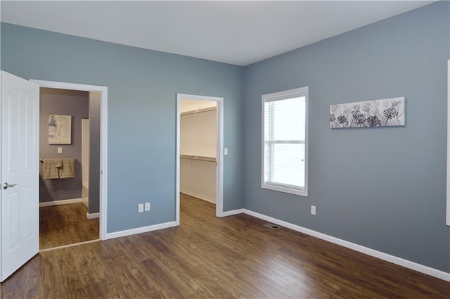 unfurnished bedroom featuring a walk in closet, dark hardwood / wood-style flooring, and a closet