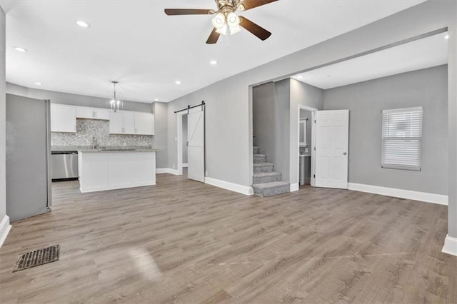 unfurnished living room with a barn door, ceiling fan, and light wood-type flooring