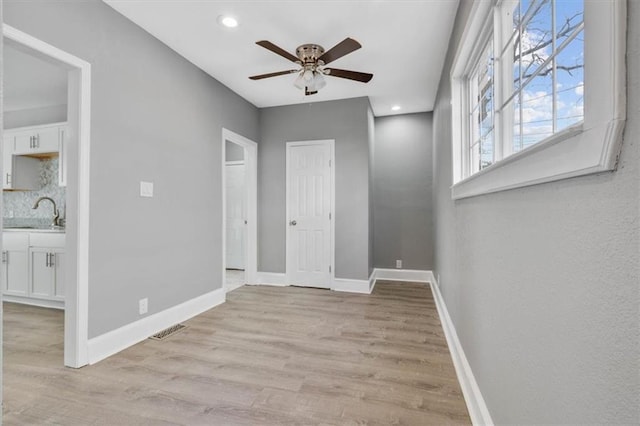 empty room featuring ceiling fan, sink, and light wood-type flooring