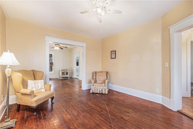 living area with dark hardwood / wood-style floors, ceiling fan, and a wood stove