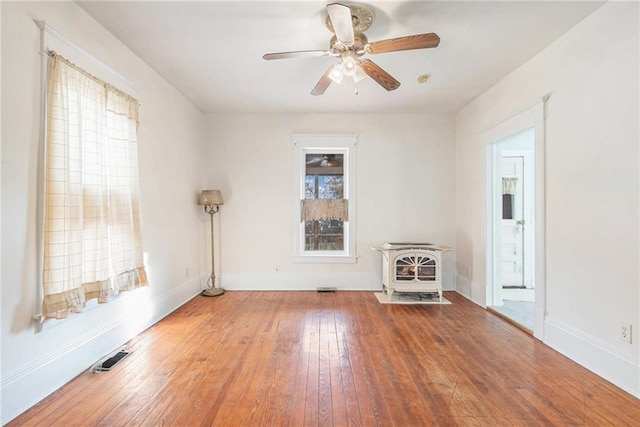 empty room featuring visible vents, a wood stove, ceiling fan, and hardwood / wood-style flooring