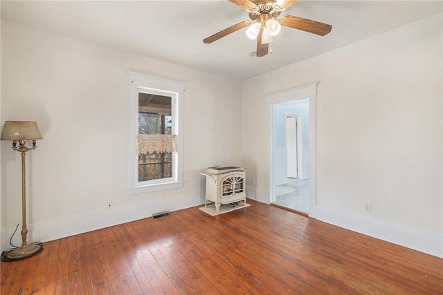 spare room featuring visible vents, a wood stove, hardwood / wood-style flooring, and baseboards