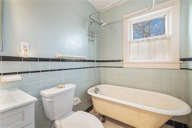 full bath with a freestanding tub, vanity, toilet, wainscoting, and tile walls