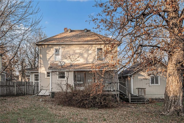 rear view of house with fence and a shingled roof