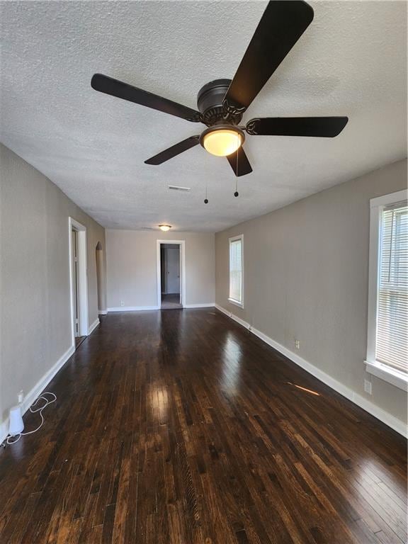 empty room featuring a textured ceiling, dark wood-type flooring, ceiling fan, and a healthy amount of sunlight