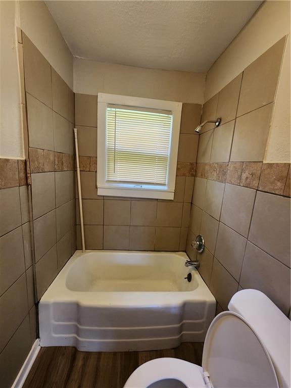 bathroom featuring a textured ceiling, tiled shower / bath combo, wood-type flooring, tile walls, and toilet