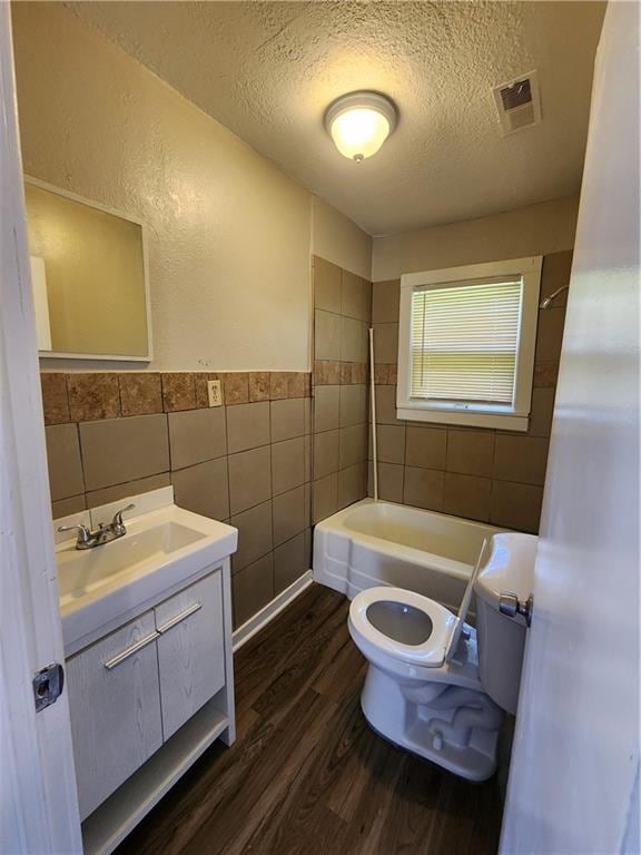 full bathroom with hardwood / wood-style floors, vanity, toilet, tile walls, and a textured ceiling