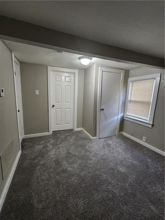 spare room featuring a textured ceiling and dark colored carpet