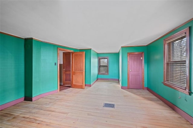 spare room featuring baseboards, visible vents, wood finished floors, and ornamental molding