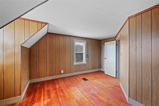 additional living space featuring wood-type flooring, vaulted ceiling, and wood walls