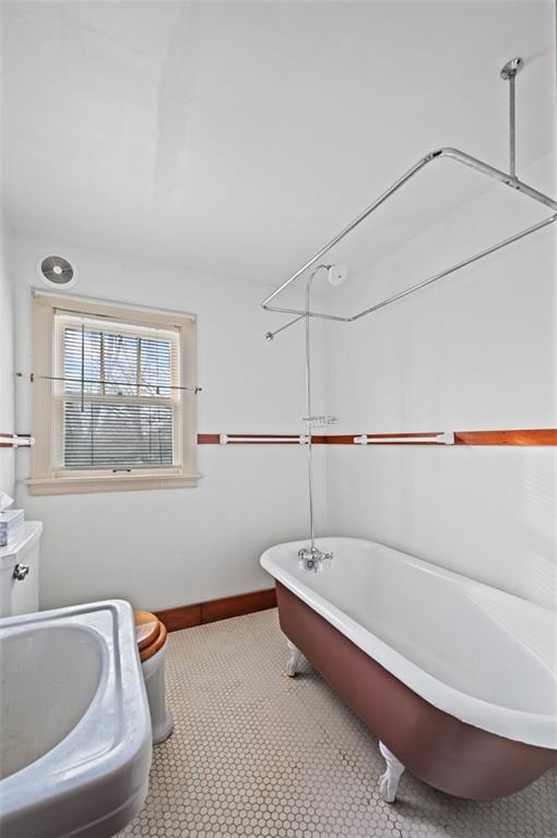 full bath featuring a sink, a freestanding tub, toilet, and baseboards