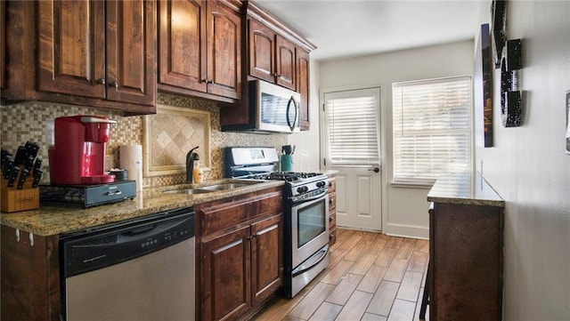 kitchen featuring appliances with stainless steel finishes, light wood-type flooring, backsplash, light stone counters, and sink