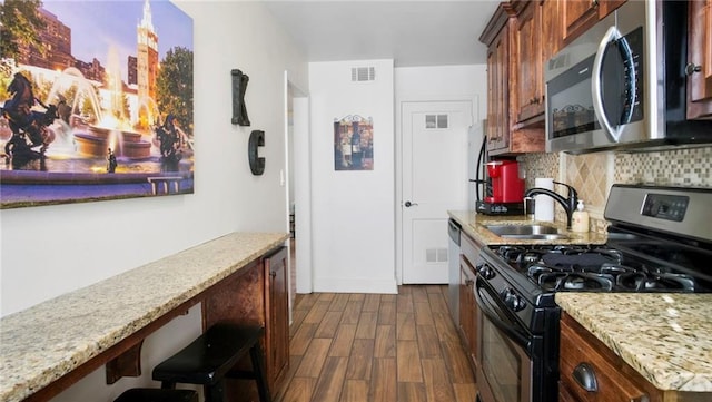 kitchen with dark wood-type flooring, black gas stove, sink, decorative backsplash, and light stone countertops