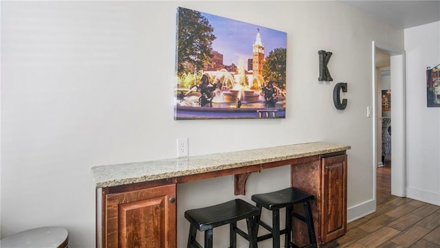 bar with light stone counters, built in desk, and dark hardwood / wood-style floors