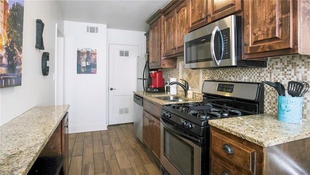 kitchen featuring decorative backsplash, appliances with stainless steel finishes, dark hardwood / wood-style flooring, light stone countertops, and sink