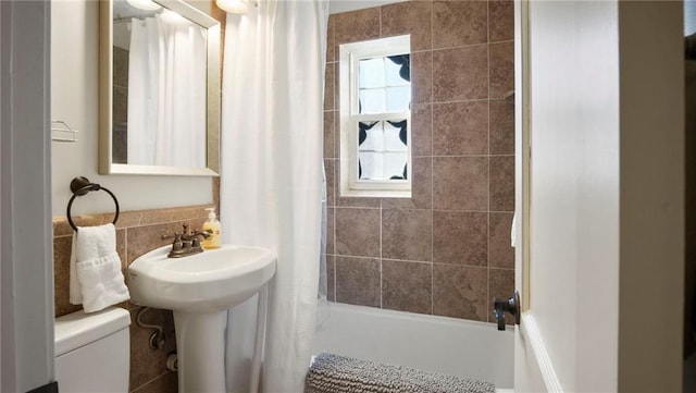 bathroom with toilet, shower / bathtub combination with curtain, and tile walls