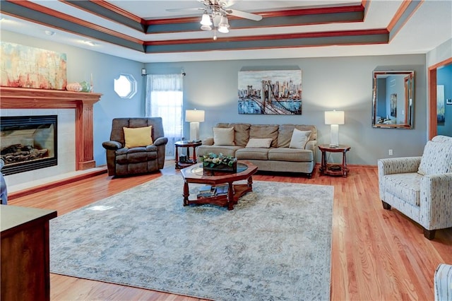 living room featuring a raised ceiling, a tile fireplace, and light wood-type flooring