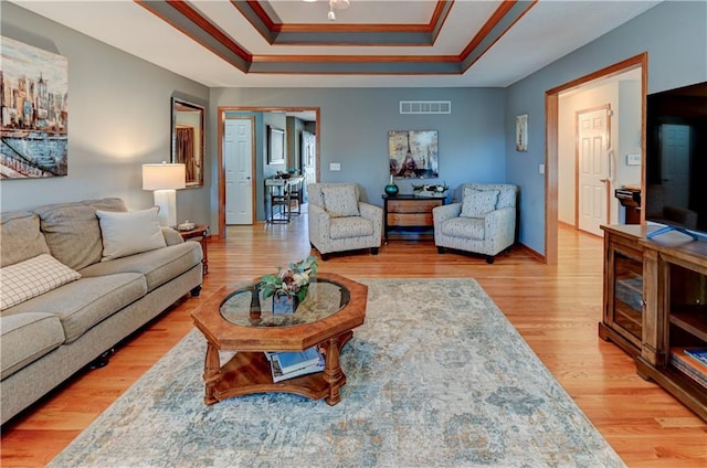 living room with wood-type flooring, crown molding, and a tray ceiling