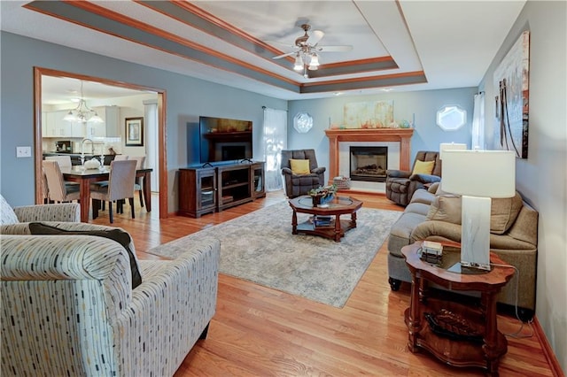 living room featuring ceiling fan with notable chandelier, light hardwood / wood-style floors, and a tray ceiling