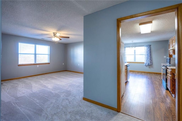 empty room featuring plenty of natural light, ceiling fan with notable chandelier, a textured ceiling, and light hardwood / wood-style flooring