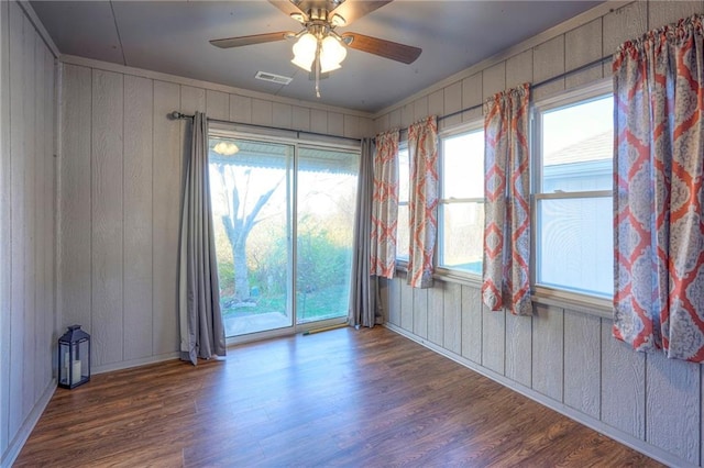 unfurnished room featuring dark hardwood / wood-style flooring, ceiling fan, and wooden walls